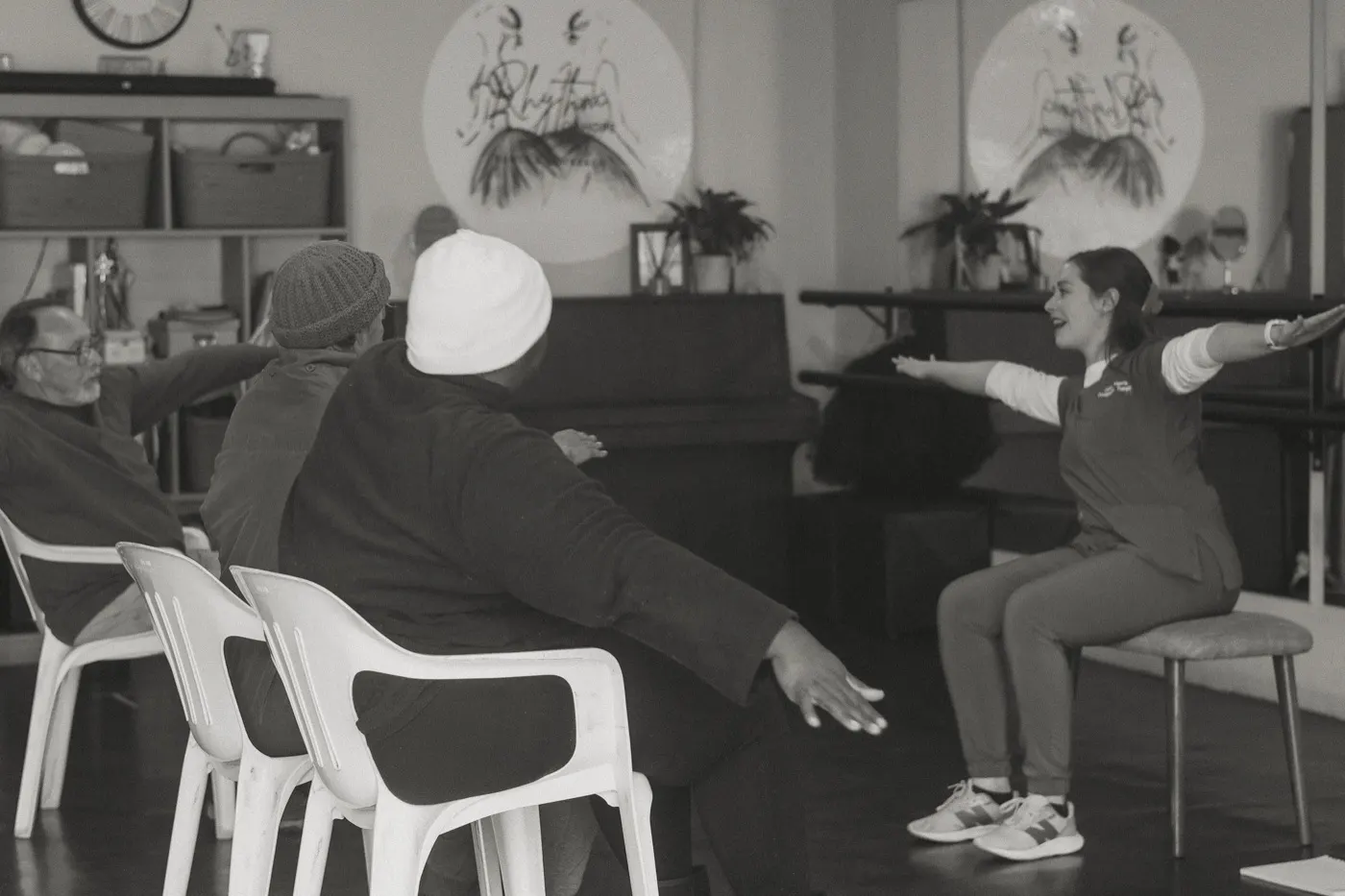 Seated class members reaching their arms out to the side as the therapist leads from the front.