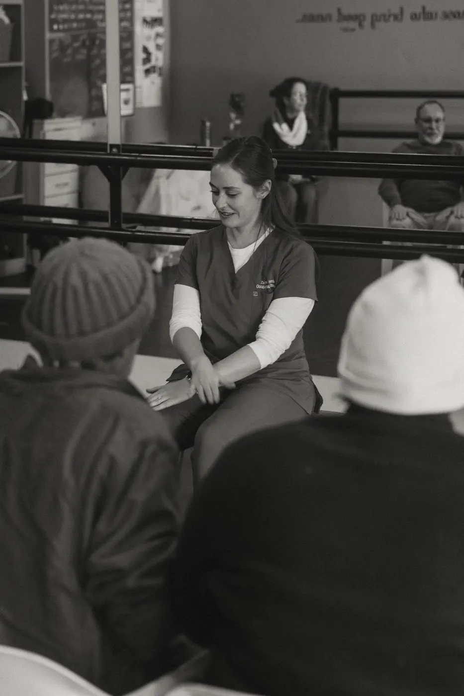 Therapist smiling as she guides two seated participants through a hand exercise.