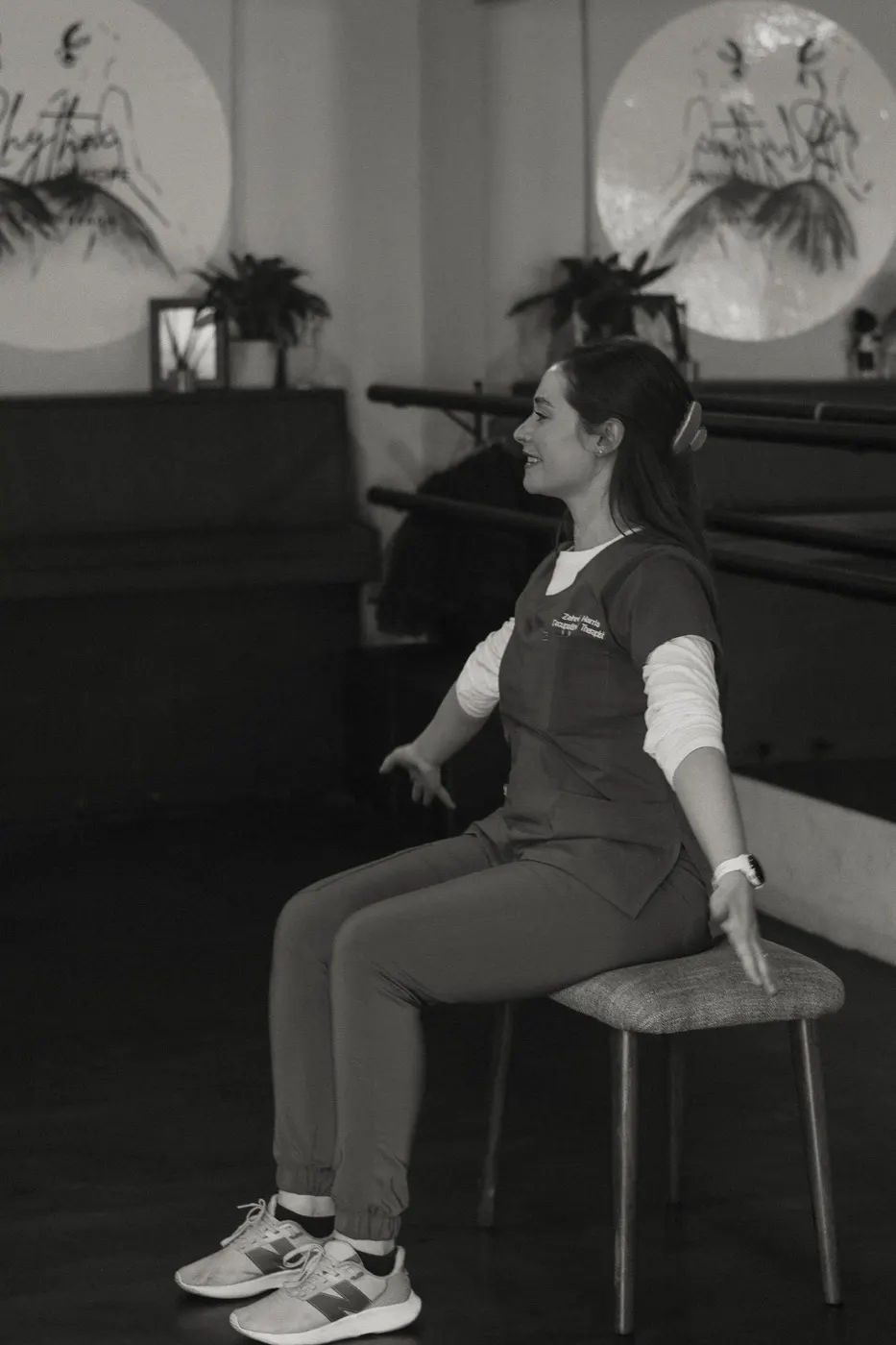 Therapist seated and smiling while leading a relaxed seated movement.